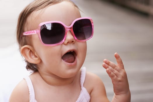 Baby, laugh and sunglasses outdoor with summer, youth fashion and young girl on holiday. Kid, fun frames and happy on vacation with shades style, child clothes and trendy accessory of toddler.