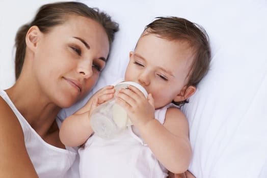 Baby, mother and drinking bottle for nutrition, liquid food and relaxing together on bed at home. Mommy, toddler and formula for health or child development in bedroom, feeding and milk for wellness.