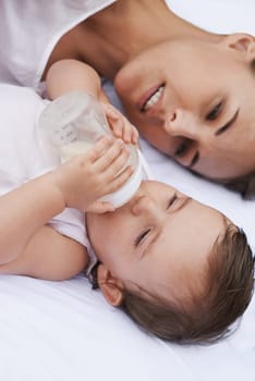 Above, care and a mother with a baby and milk for nutrition, health and growth development. Morning, family and a young mom and child with a bottle in the bedroom of a house for food and a drink.