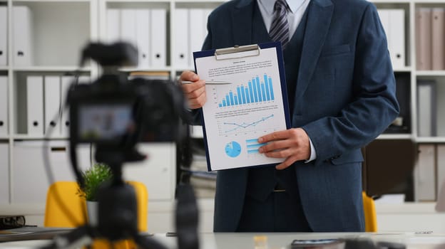 Male in suit and tie show stats graph pad making promo videoblog or photo session in office camcorder to tripod closeup. Vlogger selfie sale solution or finance advisor management information