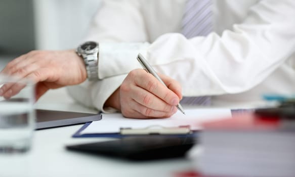 Male arm in suit and tie hold silver pen filling schedule in notepad at office workplace closeup. Legal law consult assistance gesture or finance investment advisor clerk job information gesture