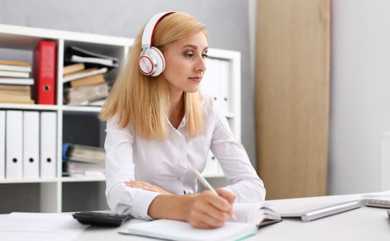 Beautiful female student with headphones listening to music and learning. Hold the pen in his hand and looking at camera