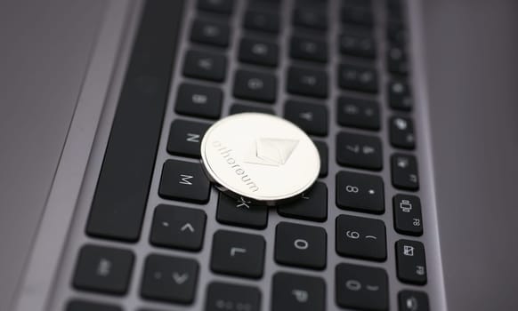 Silver ethereum coin is lying on laptop pc keyboard closeup. Future web ico new money type eth btc free fast trade concept