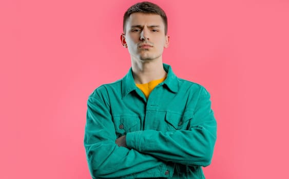 Offended upset young guy with arms crossed feeling mad at someone. Teen maximalism. Facial expressions, emotions and feelings. Body language. Self-confident man on pink background.