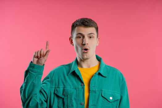 Smart young man having idea eureka moment, pointing finger up on violet background. Smart student guy showing answer gesture or remembered what he forgot, memory concept.