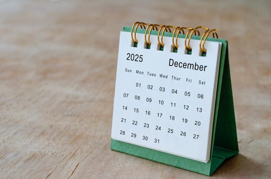 December 2025 table calendar on wooden desk with customizable space for text. Copy space and calendar concept.