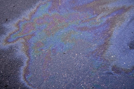 Oil stain on the asphalt, rainbow-shaped colored gasoline stains on an asphalt road as a texture or background. Oil spill on dark asphalt, parking lot.