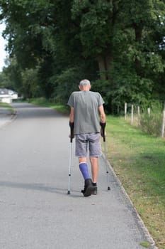 A man with a broken leg is walking down the street, on his left leg he has a special boot for walking, if the leg is in a cast, the man moves with the help of crutches,high quality photo