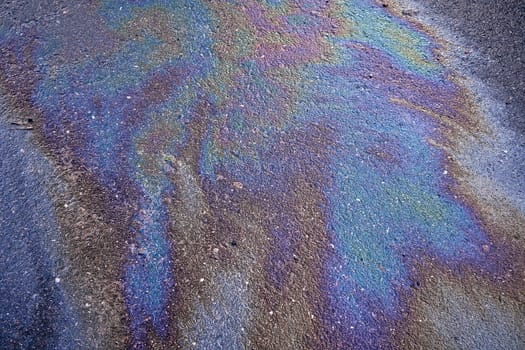 A puddle of spilled gasoline or oil product on the road. Environmental pollution concept. Gasoline flows on the asphalt. Rainbow stains of oil and gasoline.