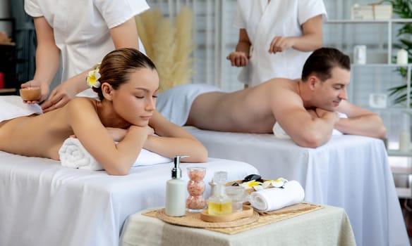 Blissful couple customer having exfoliation treatment in luxury spa salon with warmth candle light ambient. Salt scrub beauty treatment in health spa body scrub. Quiescent