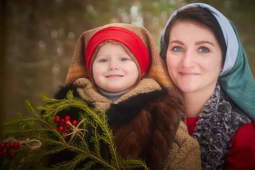 Family with mother and little daughter in stylized medieval peasant clothing in winter forest. The woman and child pose for fairy tale photoshoot in nature on a cold day. Concept of love, friendship