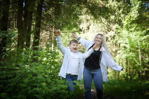 Funny mother with dreadlocks and fat boy happy walking in the forest on a sunny summer day