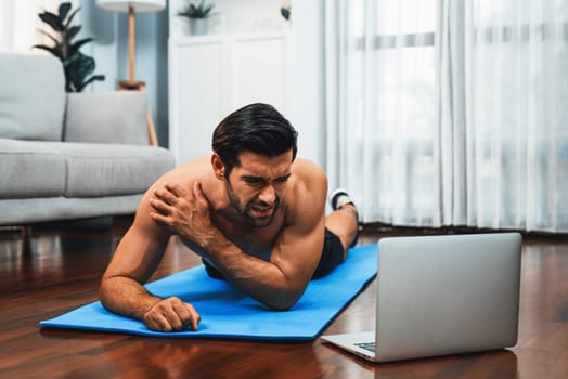 Athletic and sporty man suffer from exercise injury during online body workout exercise session at home. Painful ache from injured muscle accident during gaiety home exercise workout training concept.