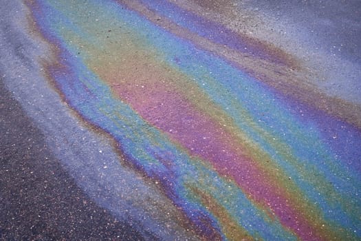 Background texture of an oil spill in the form of a rainbow stain on dark asphalt, parking. Selective focus