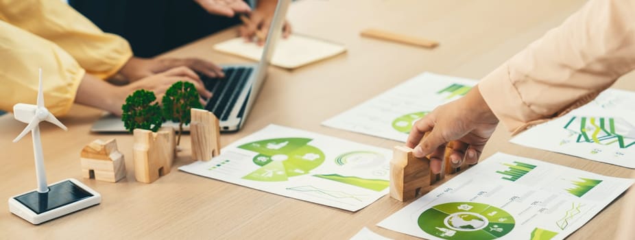 Environmental documents and a windmill model representing the use of clean energy are scattered on the table during a green business discussion about investing in clean energy. Closeup. Delineation.