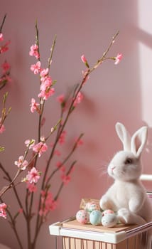One shopping cart with one toy Easter bunny sits on a gift box with Easter eggs in a shopping cart, and next to it are blooming sakura branches on a pink background, side view close-up.
