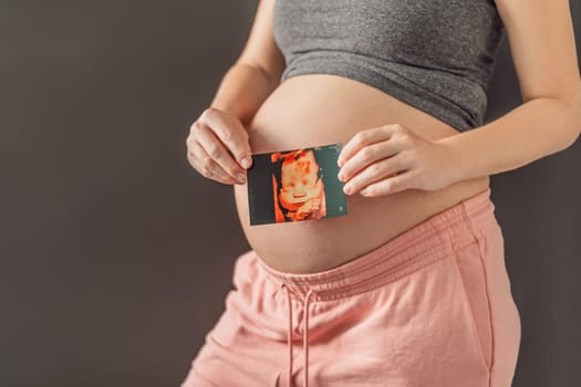 Expectant mother tenderly connects with her unborn child, holding ultrasound photo to her pregnant belly.