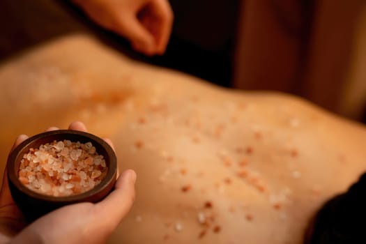 Closeup man customer having exfoliation treatment in luxury spa salon with warmth candle light ambient. Salt scrub beauty treatment in Health spa body scrub. Quiescent