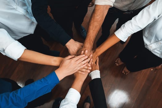 Group of diverse office worker join hand together in office room symbolize business synergy and strong productive teamwork in workplace. Cooperation and unity between business employee. Prudent