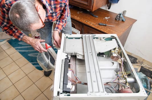 middle-aged master in a checkered suit unscrews the lid of a washing machine with a screwdriver for repair, repairs washing machines and household appliances at home, high quality photo