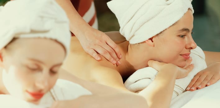 A couple of beautiful young woman with white towel lie on comfortable spa bed during receive relaxing body massage by professional masseur surrounded at spa salon. Gray background. Tranquility.