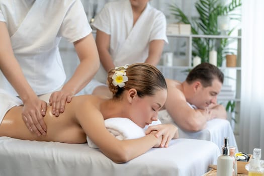 Caucasian couple customer enjoying relaxing anti-stress spa massage and pampering with beauty skin recreation leisure in day light ambient salon spa at luxury resort or hotel. Quiescent