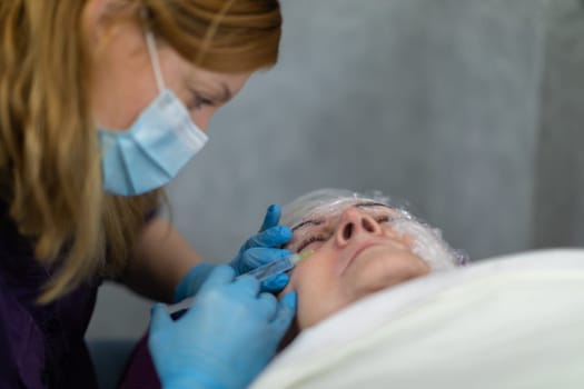 Close-up of cosmetologist's face and hands at work. A woman working in an aesthetic medicine salon performs a treatment on a client.