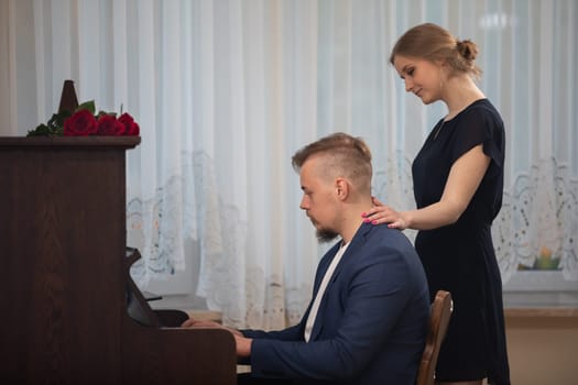 A man playing the piano without notes. A man performs a piano piece from memory. He is dressed in an elegant suit. Women's hands stroke the man's shoulders.
