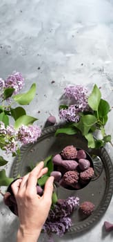 woman's hand takes cuberdon praline from a candy bowl, Belgian sweets in glasses, spring still life with a lilac branch, top view, High quality photo