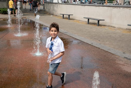 Boy playing with fountain in public park, child having fun, dancing, having fun in hot summer, leisure concept, High quality photo