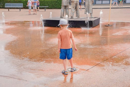 Boy playing with a fountain in a public park, she is having fun, dancing, hot summer fun, leisure concept, rear view, Lommel, Belgium - June 17, 2023, High quality photo