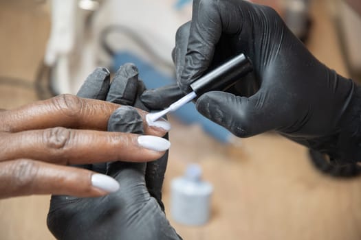 Manicurist covers the nails of a dark-skinned girl with blue gel polish in a beauty salon, High quality photo