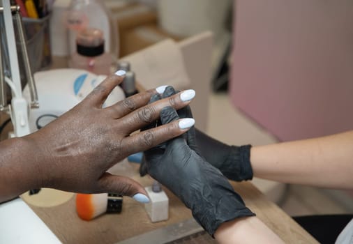 Manicurist covers the nails of a dark-skinned girl with blue gel polish in a beauty salon, High quality photo