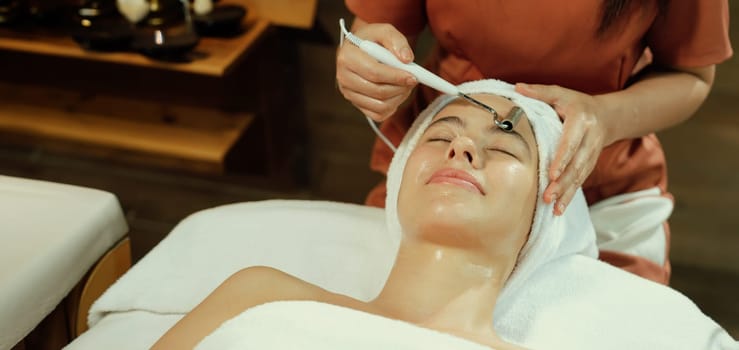 Beautiful caucasian woman lying on spa bed during having facial massage by professional hands at modern spa salon surrounded by beauty electrical equipment or medical equipment. Close up. Tranquility