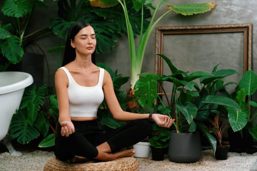 Young woman doing morning yoga and meditation in natural garden with plant leaf, enjoying the solitude and practicing meditative poses. Mindfulness activity and healthy mind lifestyle. Blithe