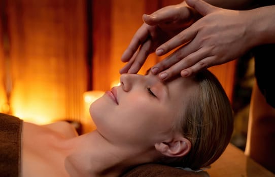 Closeup caucasian woman enjoying relaxing anti-stress head massage and pampering facial beauty skin recreation leisure in warm candle lighting ambient salon spa in luxury resort or hotel. Quiescent