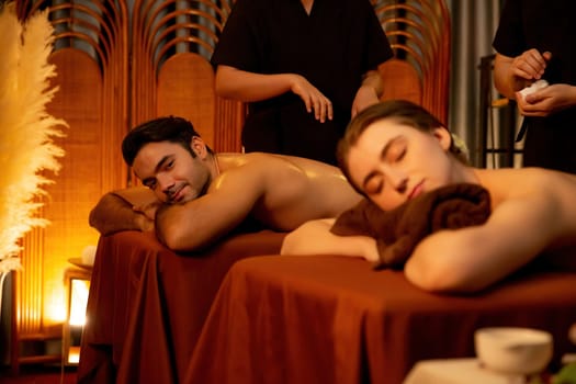 Caucasian couple customer enjoying relaxing anti-stress spa massage and pampering with beauty skin recreation leisure in warm candle lighting ambient salon spa at luxury resort or hotel. Quiescent