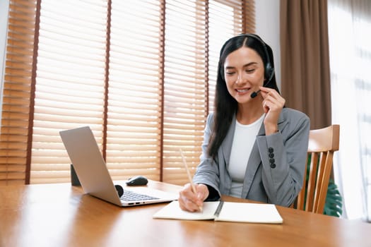 Female call center operator or customer service helpdesk staff working on workspace while talking on the headset to provide assistance for customer. Professional modern business service. Blithe