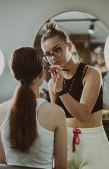 One young handsome Caucasian makeup artist applies shadows to the upper eyelid of a girl sitting in a chair from the back early in the morning in a beauty salon, close-up side view. Step by step.