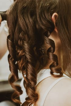 Beautiful twisted curls on the long brown hair of a young girl, close-up side view.