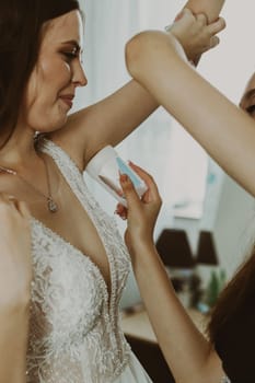 A young girl helps a happy bride apply antiperspirant to her armpits, side view, close-up.