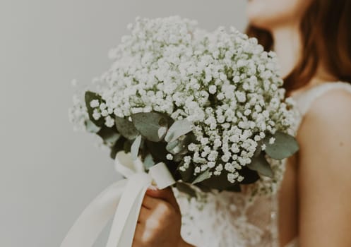 Portrait of an unrecognizable young Caucasian bride in a white dress and veil holding a wedding bouquet with white boutonnieres in front of her, bottom view.