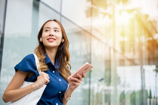 Happy young woman using wireless earbuds and smartphone for virtual chat and social media. This portrait shows a person's modern lifestyle.