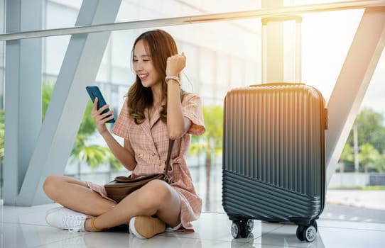 A tourist girl sitting on the ground, using her smartphone to plan her voyage. She's surrounded by luggage and ready for her adventure. Travel is her passion.