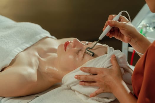 Beautiful young women lie on spa bed while having facial massage from professional doctor. Attractive female with beautiful skin surrounded by electric facial machine. Tranquility.