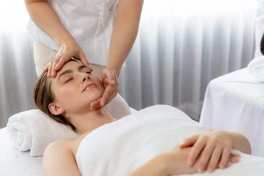 Caucasian woman enjoying relaxing anti-stress head massage and pampering facial beauty skin recreation leisure in dayspa modern light ambient at luxury resort or hotel spa salon. Quiescent