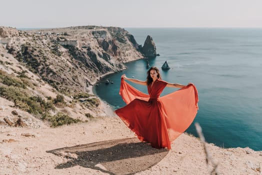 Woman red dress sea. Female dancer posing on a rocky outcrop high above the sea. Girl on the nature on blue sky background. Fashion photo