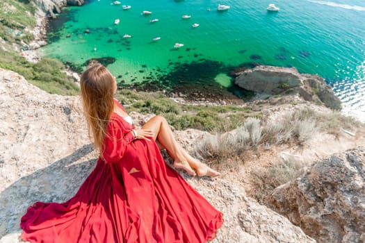 Woman red dress sea. Happy woman in a red dress and white bikini sitting on a rocky outcrop, gazing out at the sea with boats and yachts in the background