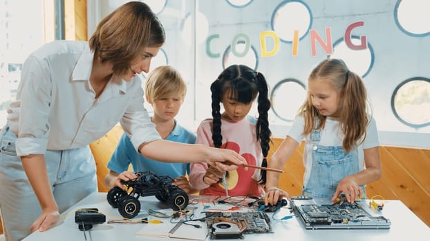 Young smart caucasian teacher teaching diverse students about electronic board. Multicultural children learn about digital electrical tool and fixing motherboard by using chips and wires. Erudition.