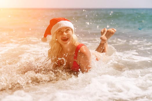 Female beach Santa hat wave coast. beach relaxation seaside. A woman in a red swimsuit enjoying her time on the beach, lying on the sand and being covered by a wave